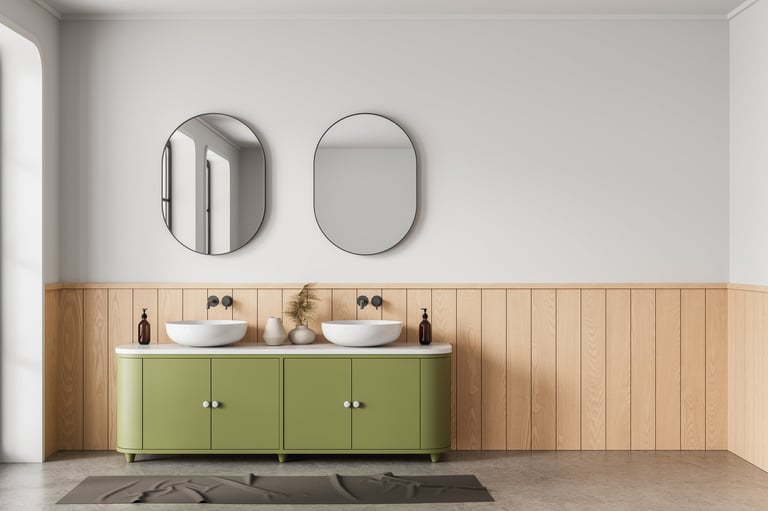 Contemporary bathroom interior with olive green vanity, two vessel sinks, oval mirrors, and wood paneling on light wall.