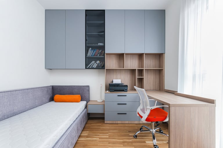 A bright room showcases a modern home office featuring a sleek workspace, a cozy daybed, and organized shelves filled with books.