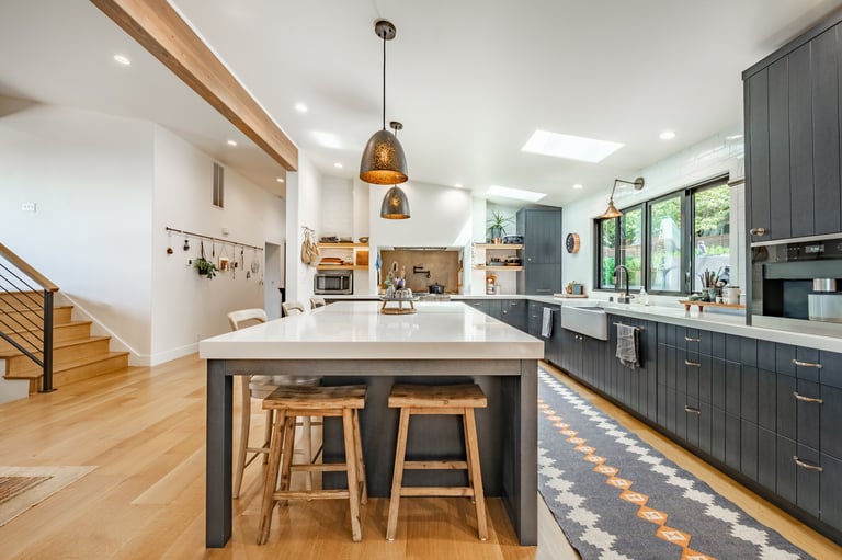 A modern kitchen with dark cabinetry light countertops warm wood flooring. Featuring a large central island with white countertop and seating.