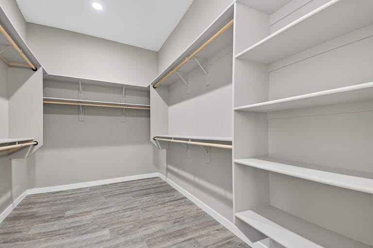 Spacious walk-in closet with custom built-in shelving, hanging rods, and wood-look laminate flooring — custom storage at its finest.